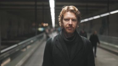 Kızıl saçlı neşeli bir adamın portresi. Havaalanında ya da metroda yürüyen bir yolda seyahat ediyor.