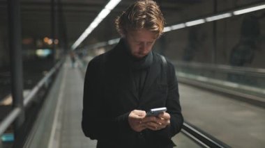 Havaalanının kaldırımında dikilirken cep telefonuyla mesaj atan beyaz bir erkek.