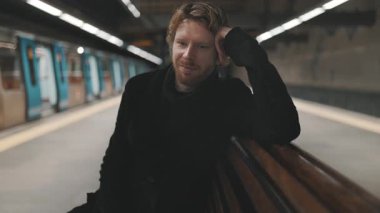 Kızıl saçlı düşünceli genç bir adam boş bir metro istasyonunda tek başına oturuyor.