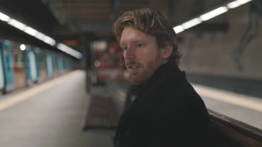 Bir metro istasyonunda bankta otururken sakallı yakışıklı beyaz adam konuşuyor.