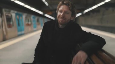 Rahat genç adam metro istasyonunda bir bankta tren hareket ederken bekliyor.