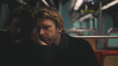 Melankolik bir adam gece trenle gidip geliyor, düşüncelere dalmış ve penceredeki görüntüsünü yansıtıyor.