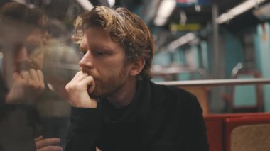 Düşünceli ve endişeli bir adam metroya binerken pencereden dışarı bakıyor.