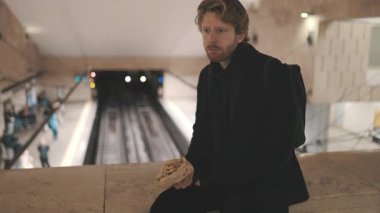 Tedirgin bir adam sırt çantalı metro istasyonunda oturmuş trenin gelmesini bekliyor.
