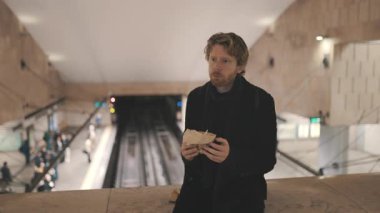 Adam metropolitan metro istasyonunda toplu taşıma beklerken yemek yiyor.