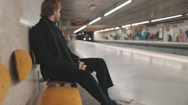 Tren istasyona varırken metro istasyonunda oturan melankolik adam.