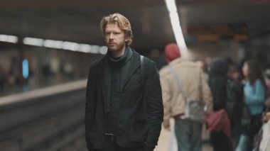 Kalabalık bir metro istasyonunda tek başına treni bekleyen ciddi bir gencin portresi.