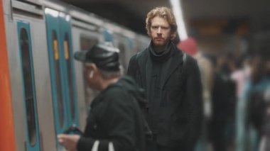 Kızıl saçlı yakışıklı genç adam metro istasyonunda tren bekliyor.