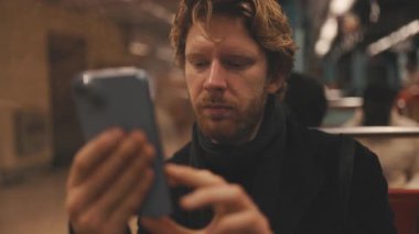 Odaklanmış bir adam, sosyal medyada veya mesajlarda cep telefonuyla metroya gidip geliyor.