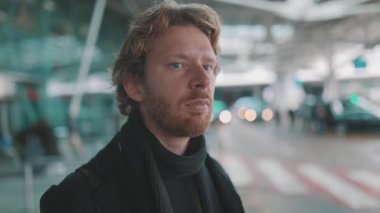 Havaalanının dışında bekleyen sakallı, ciddi bir adam.