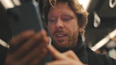 Sakallı, beyaz bir adam metroda cep telefonuyla mesaj atıyor.