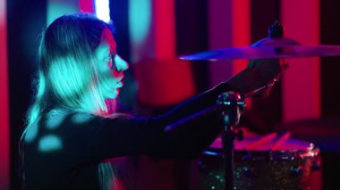 Tutkulu genç bir kadın, neon ışıkları olan karanlık bir kulüpte canlı müzik performansı sırasında davul çalıyor.