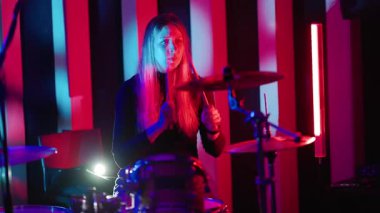 Kırmızı ve mavi neon ışıkları olan bir stüdyoda tutkuyla davul çalan genç bir kadın.