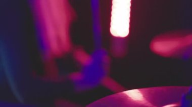 Canlı pembe ve mavi ışıklarla dolu bir konser sırasında güçlü bir şekilde davul çalan tanınmayan bir kadın.