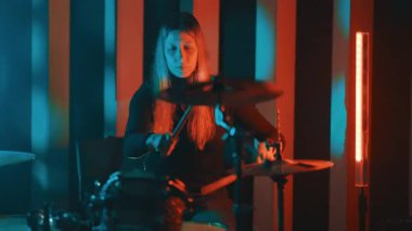 Profesyonel bayan müzisyen, renkli ışıklarla karanlık bir müzik stüdyosunda davul solosu yapıyor.