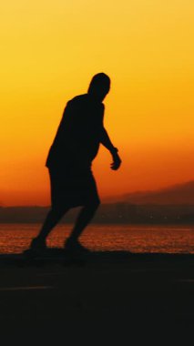 Gün batımında kaykay yapan bir adamın silüeti. Orta çekim
