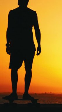 Gün batımında kaykayla kayan genç bir adamın silueti. Orta çekim