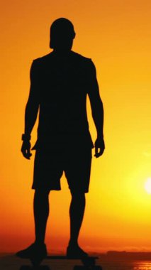 Gün batımında sörf tahtasında kayan atletik bir adamın silueti. Orta çekim