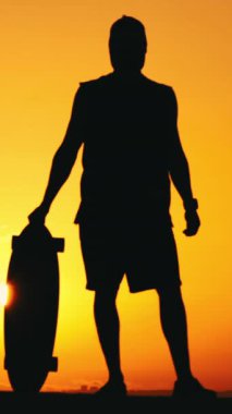 Gün batımında elinde uzun tahta tutan bir adamın silüeti. Orta çekim