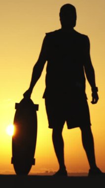 Gün batımında duran ve omzuna uzun tahta takan bir delikanlının silueti. Orta çekim