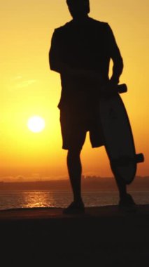 Gün batımında kaykayla kayan genç bir atletin silüeti.
