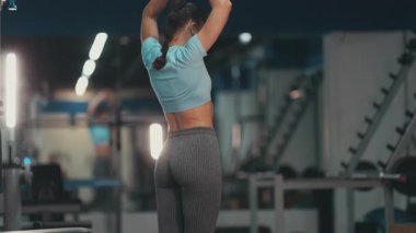 Formda bir kadın spor salonunda egzersiz yapmadan önce ısınma egzersizleri yapıyor ve kollarını geriyor.