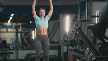Formda bir kadın, güç antrenmanı sırasında dambıllarla omuz egzersizi yapıyor.