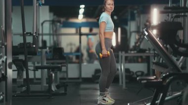 Kararlı bir kadın modern bir fitness kulübünde güç eğitimi için dambıllarla hamle yapıyor.