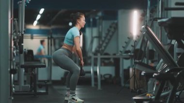 Atletik kadın bir fitness kulübünde bacak ve kalça egzersizi için çömelme hareketi yapıyor.