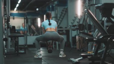 Atletik kadın bir spor salonunda kalça kasları ve bacak dayanıklılığı eğitimi için sumo yapıyor.