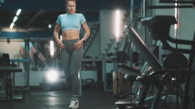 Genç atletik kadın spor aletleriyle modern bir spor salonunda spor yapmaya hazırlanıyor.