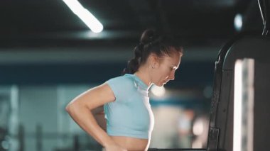 Modern bir spor salonunda, güçlü bir kadın paralel bar makinesinde trisepslere daldırma egzersizi yapıyor.