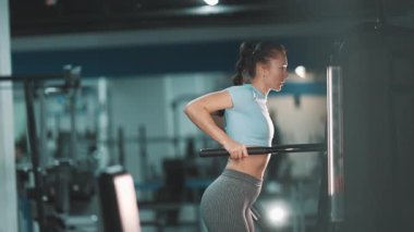 Genç atletik bir kadın destek makinesine triseps batırma egzersizi yapıyor.