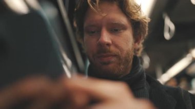 Bir metro treninde işe gidip gelen uykulu genç işadamı telefonuna bakarken gözlerini ovalıyor.