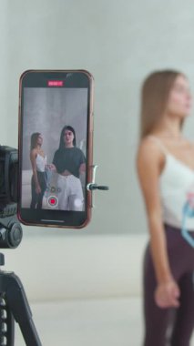 Sağlık ve kilo kaybıyla ilgili bir video blogu için video çekmek - kamerada konuşan genç bir kadın ve kamerada ince bir modelin vücudunun ölçümünü alıyor. Orta çekim