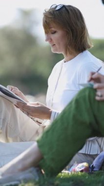 Parktaki defterlerinde çizim yapan iki gülümseyen kadın. Orta çekim