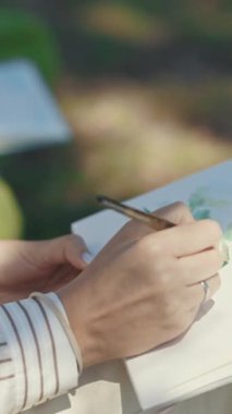 Sanatçıların el ve çarşaf resimlerinin yakın çekimleri parkta suluboya bir manzara çiziyor. Orta çekim