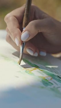 Bir kadın doğada dalları suluboya ile boyar. Orta çekim