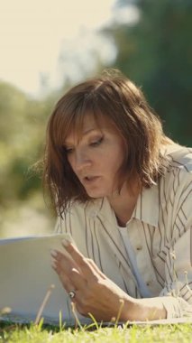 Bir kadın sanatçı çimlerin üzerinde uzanıyor, çiziyor ve konuşuyor. Orta çekim