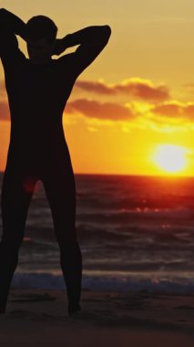 Bir adam dalgıç kıyafetini bağlar ve kumdan sörf tahtasını kaldırır. Parlak günbatımı. Orta çekim