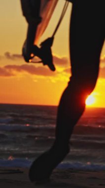 Okyanusun üzerinde parlak turuncu bir günbatımının arka planında sörfçü bacakları. Orta çekim