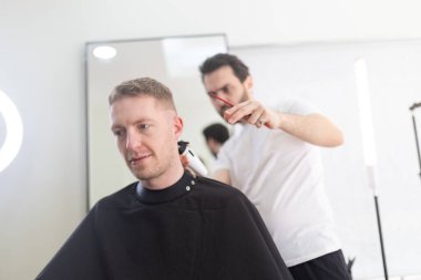 Temiz, çağdaş bir kuaför salonunda berberden yeni saç kesimi alan bir adam.