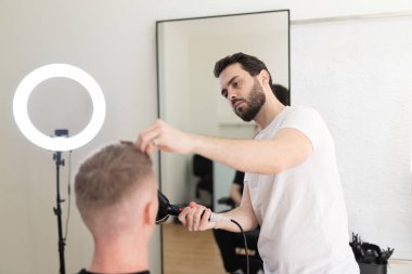 Profesyonel erkek berber saç kurutma makinesiyle müşterilerin saçını şekillendirmeye odaklanıyor.