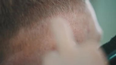 Profesyonel bir berbere yakın çekim. Müşterileri tıraş makinesiyle kısa saç kesiyor.