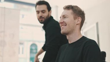 Modern bir kuaförde saç kesiminden önce gülümseyen bir erkek müşteriye pelerin takan profesyonel bir kuaför.