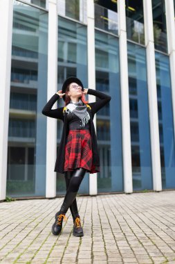 Şık bir kadın şehir ortamında kendine güvenerek duruyor, şık kıyafetler giyiyor.