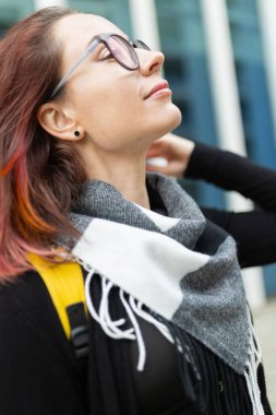 Genç bir kadın başını arkaya yaslayarak iyi hissediyor, pozitif şehir atmosferini kucaklıyor.