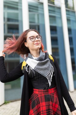 Gülümseyen, gözlüklü, ekose etekli genç bir kadın.