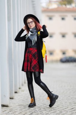 Parlak sarı bir sırt çantasıyla şık bir sokakta poz veren genç bir kadın.