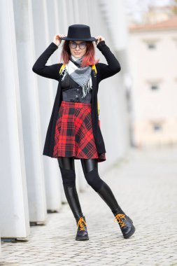 Genç bir kadın kendine güvenerek şapkasını düzeltiyor, alternatif sokak tarzı bir kıyafet sergiliyor.